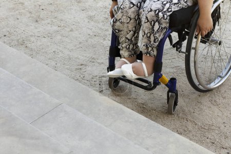 Foto de Mujer adulta discapacitada joven recortada en silla de ruedas frente a la escalera en Sandy Path. Sensibilización sobre las barreras arquitectónicas y los problemas de accesibilidad. Copiar espacio para texto, plano horizontal. - Imagen libre de derechos