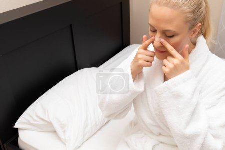 White Woman applique la bande nasale sur le nez avant d'aller au lit, assis sur le lit. Arrêtez sans drogue, ronflement, solution d'apnée du sommeil. Espace de copie. Bandage adhésif pour une meilleure respiration saine. Horizontal