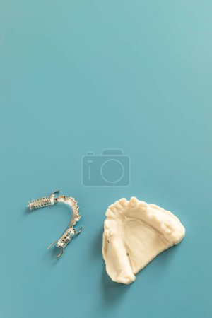 Metal Frame Lower Partial Denture with Die Stone, Plaster Cast Molds Of Lower Jaws, Cobalt Chrome Dental Plate, Flat Lay Mockup 3D Printed Bridge On Blue Background. Copy Space. Vertical Plane