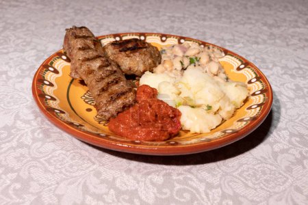 Teller mit traditioneller bulgarischer Küche vorhanden. Kartoffelpüree, Gemüsegericht Ljutenica, weiße Bohnen, Haricot, Hackfleisch vom Grill mit Gewürzen Kebapche. Horizontale Ebene. Hochwertiges Foto