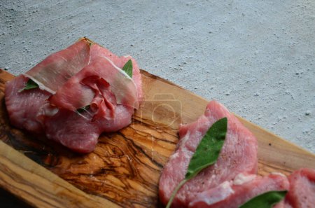 Saltimbocca de veau préparé enveloppé de jambon séché à l'air et de feuilles de sauge sur une planche de cuisine 
