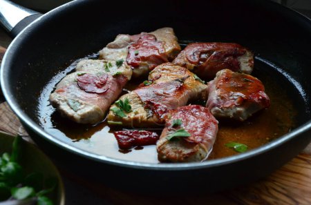 Prepared veal saltimbocca wrapped with air-dried ham and sage leaves on a kitchen board 