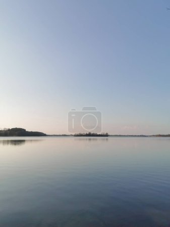 Foto de Vista del lago al atardecer. Agua azul calma, horizonte y cielo despejado. Escena de tranquilidad de la naturaleza. Espacio para el texto. Foto vertical. - Imagen libre de derechos