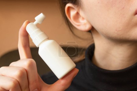 White ear spray bottle with nozzle in woman's hand. For daily clean the ears from earwax. Woman's hygiene and health care. Horizontal photo. Close-up.