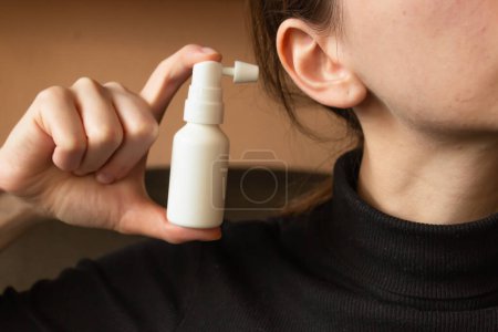 Woman shows how to use an ear spray. White plastic bottle with nozzle to clean the ears from earwax. Daily ear care and hygiene. Horizontal photo. Close-up.
