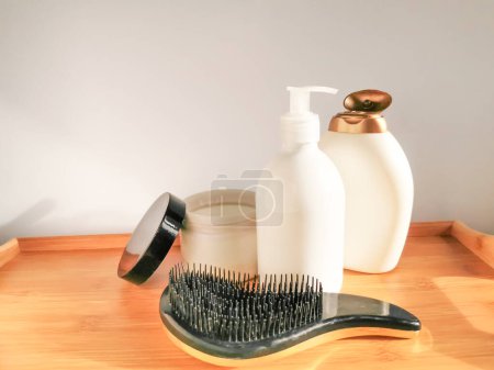 Foto de Hair care set: two white bottles of shampoo and conditioner, hair brush and open jar of hair mask with golden details on the wooden table. - Imagen libre de derechos