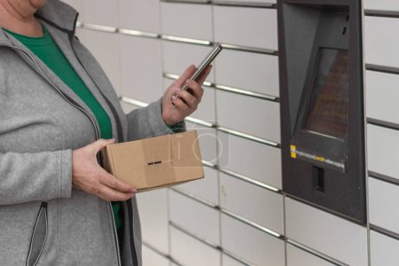 Pniewy, Polen - 22. März 2023. Seniorin mit Smartphone-Eingabecode öffnet Spind im Postzustelldienst für Empfänge oder sendet eine Schachtel. E-Commerce-Versand- und Lieferkonzept.