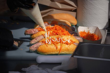 Photo for Cook pours mayonnaise over ready-made hot dogs. Street food - Royalty Free Image