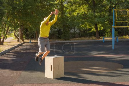 Photo for Man jumps over a wooden box while exercising at an outdoor sports ground. Healthy lifestyle - Royalty Free Image