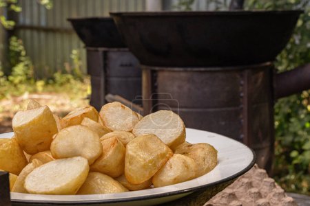 Photo for Fried large potatoes against the backdrop of outdoor cauldrons mounted on metal wood-burning stoves - Royalty Free Image