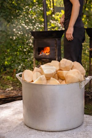 Photo for Coarsely chopped potatoes for frying in a cast iron cauldron against the backdrop of an oven with burning wood. Street food - Royalty Free Image
