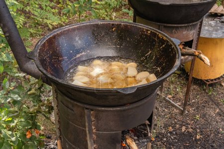 Photo for Coarsely chopped potatoes are fried in boiling oil in a cast-iron cauldron on a wood-burning stove. Street food - Royalty Free Image