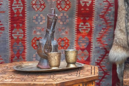 Téléchargez les photos : Des cruches asiatiques traditionnelles et des tasses en argent se dressent sur une vieille table en bois dans une yourte - la maison des nomades. - en image libre de droit