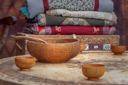 Téléchargez les photos : Les ustensiles traditionnels asiatiques en bois pour les boissons au lait se dressent sur une table basse sur le fond d'un coffre avec des couvertures à l'intérieur d'une maison nomade une yourte. Gros plan - en image libre de droit