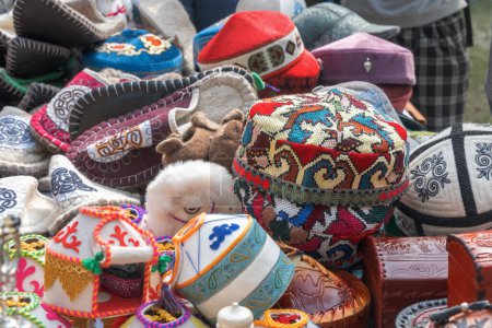 Téléchargez les photos : Chapeaux asiatiques traditionnels avec broderie nationale d'ornement et chaussures en feutre sur le comptoir d'un magasin de rue. Fait à la main - en image libre de droit
