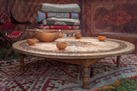 Des ustensiles en bois asiatiques traditionnels pour les boissons au lait se tiennent sur une table basse sur le fond d'un coffre avec des couvertures à l'intérieur d'une maison nomade une yourte.