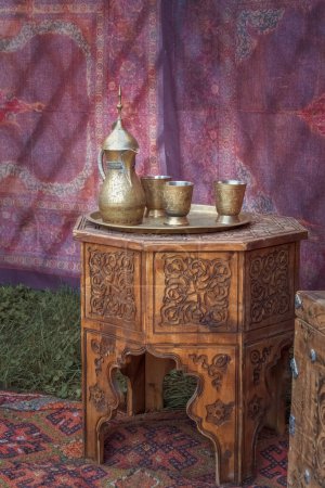 Téléchargez les photos : La cruche et les tasses traditionnelles asiatiques en argent se dressent sur une vieille table en bois dans une yourte - la maison des nomades. - en image libre de droit