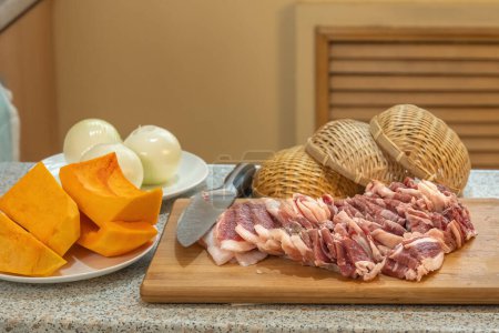 Beautifully cut slices of fresh fatty meat for further cooking on a background of bamboo utensils and vegetables.