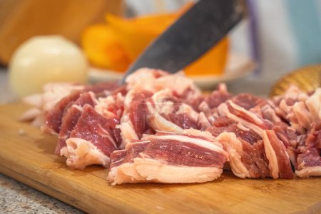 Beautifully cut slices of fresh fatty meat for further cooking on a background of bamboo utensils and vegetables. Close-up