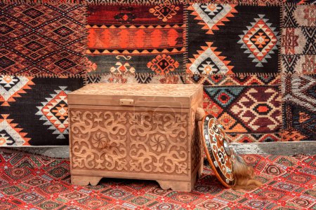 Traditional Asian wooden chest with carved ornaments against the background of carpets in a yurt - the dwellings of nomads. Close-up