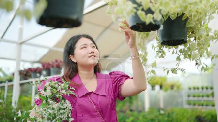 Photo for Happy young  Asian woman customer buys green plants at the garden store shop, A young lady chooses ornamental plants at a flower market, Home and Garden concept - Royalty Free Image
