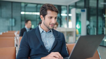 Téléchargez les photos : Gros plan sur le visage d'un bel homme d'affaires indien ou latin assis et travaillant sur un ordinateur portable en attente de vol à l'aérogare - en image libre de droit