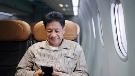 Foto de Hombre mayor de pasajeros asiáticos usando un teléfono inteligente mientras está sentado en el avión. Concepto de viaje y tecnología - Imagen libre de derechos