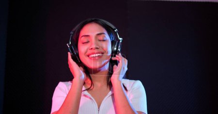 Foto de Mujer asiática feliz escuchando música en auriculares en el estudio con luces de neón - Imagen libre de derechos