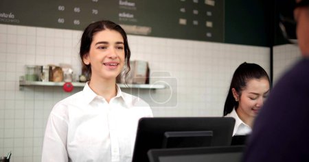 Téléchargez les photos : Femme employée de café barista travaillant au café. Caissière serveuse souriante prenant le café de commande et la boulangerie du client. Propriétaire de petite entreprise et concept de travail à temps partiel - en image libre de droit
