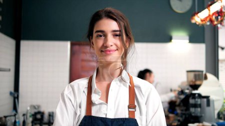Portrait of young barista wearing apron and looking at camera. Excited small business owner