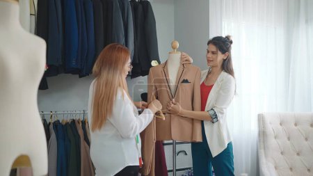 Téléchargez les photos : Deux créatrice de mode asiatique professionnelle discutant et concevant pour une nouvelle collection de costumes pour hommes au studio ou au magasin de vêtements - en image libre de droit