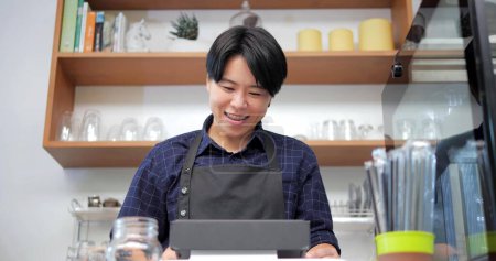 Téléchargez les photos : Happy tomboy barista utilisant la caisse à écran tactile reçoit une commande à un client au café - en image libre de droit