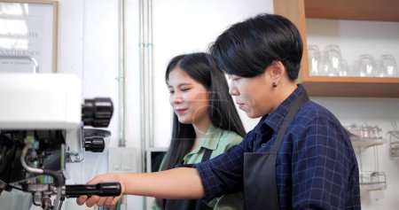 Foto de Dos mujeres asiáticas con delantales hablan y enseñan a usar la máquina de café en el restaurante cafetería - Imagen libre de derechos