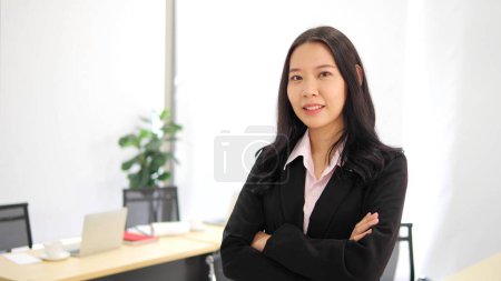 Foto de Asiática joven mujer de negocios de pie con los brazos cruzados mirando a la cámara, feliz mujer de negocios confiada líder corporativo en la oficina, foto de cerca retrato - Imagen libre de derechos