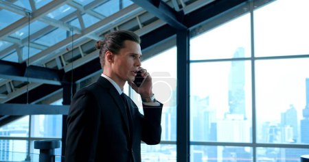 Foto de Hombre de negocios inteligente en traje hablando en el teléfono inteligente y fondo de la ventana del rascacielos - Imagen libre de derechos