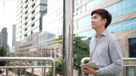 Téléchargez les photos : Portrait d'homme d'affaires asiatique heureux marchant dans la rue dans la ville moderne avec fond de bâtiment à l'extérieur - en image libre de droit