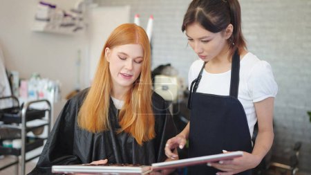 Téléchargez les photos : Les jeunes coiffeuses professionnelles discutent et recommandent des couleurs de cheveux aux clients dans le salon de coiffure - en image libre de droit