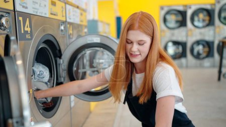 Téléchargez les photos : Jeune femme caucasienne mettre les draps dans la machine à laver au nettoyage à la blanchisserie - en image libre de droit