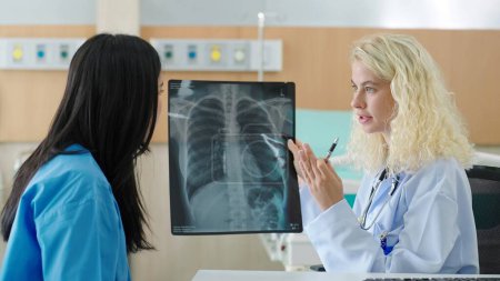 Téléchargez les photos : Médecin caucasien professionnel parlant avec une patiente de film radiographique avec pneumonie pulmonaire causée par une infection à la clinique. Test de rayons X Covid-19, épidémie mondiale de virus covid - en image libre de droit