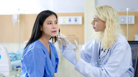 Téléchargez les photos : Femme chirurgien plastique tenant un stylo pour marque sur le visage de la patiente asiatique avant la chirurgie esthétique à la clinique - en image libre de droit