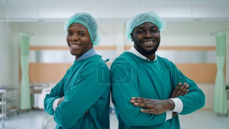 Foto de Cara sonriente de dos hombres afroamericanos médico profesional en brazos posición cruzada mirando a la cámara en el hospital - Imagen libre de derechos