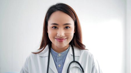 Téléchargez les photos : Portrait de jeune asiatique femme médecin portant blanc manteau stéthoscope sur les épaules sourire regarder caméra - en image libre de droit