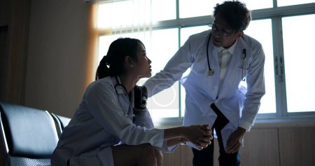 Téléchargez les photos : Asiatique homme médecins parler, réconfortant et encourageant à médecin femme elle tressailli et anxieux inquiet au sujet du traitement des patients à l'hôpital - en image libre de droit