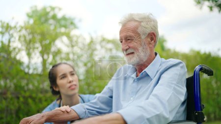 Photo for Asian female nurse caring for and helping an old man sitting in a wheelchair in the hospital garden - Royalty Free Image