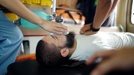 Téléchargez les photos : Un ambulancier pratiquant la RCR d'un blessé sur une civière dans la voiture d'urgence. Assistant médical utilisant un masque pour respirer - en image libre de droit