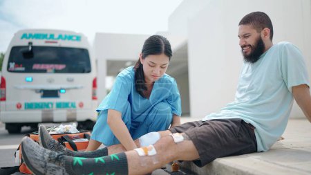 Foto de Mujer asiática paramédica médico de primeros auxilios hombre de lesionado en accidente de rodilla antes de llevar la ambulancia al hospital - Imagen libre de derechos