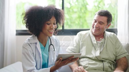 Téléchargez les photos : Médecine afro-américaine utilisant une tablette numérique expliquer les symptômes au patient après le traitement ou parler avec un patient âgé à l'hôpital - en image libre de droit