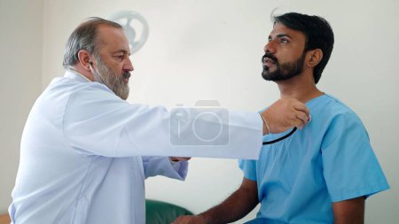 Photo for Asian senior male doctor holding examining heart by stethoscope of Indian male patient visits doctor at the hospital - Royalty Free Image