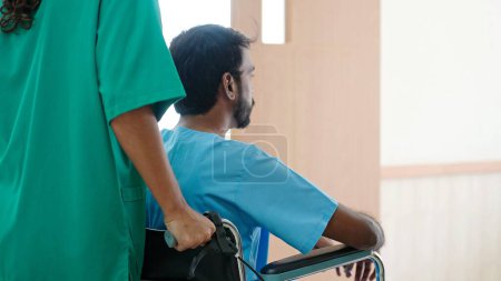 Téléchargez les photos : Vue arrière de l'infirmière poussant fauteuil roulant du patient indien masculin allant à la salle de traitement à l'hôpital - en image libre de droit