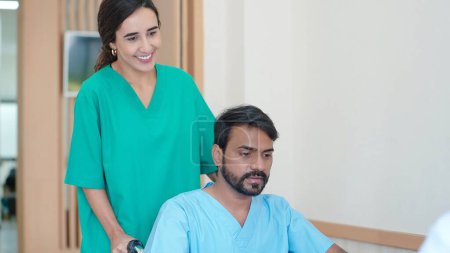 Téléchargez les photos : Jeune infirmière poussant fauteuil roulant du patient indien masculin allant à la salle de traitement à l'hôpital - en image libre de droit
